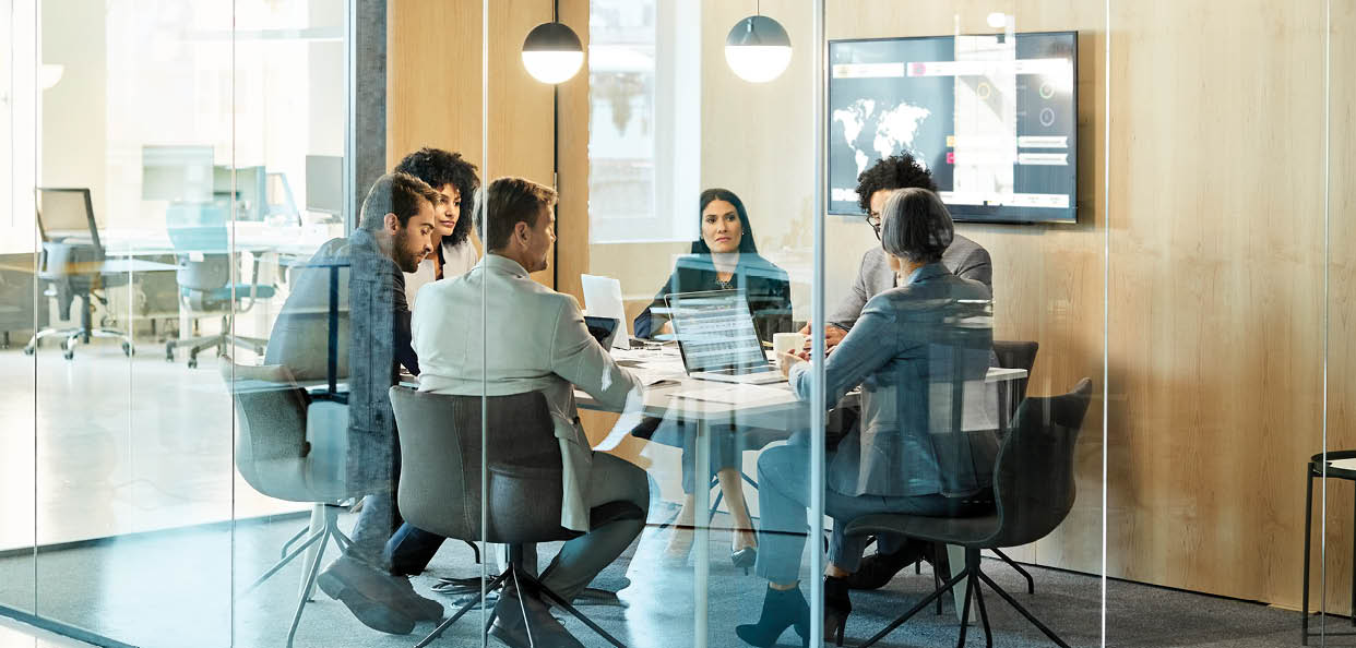 Business colleagues sitting at conference table seen through glass wall. Multi-ethnic coworkers are discussing in board room at office. They are planning strategy.