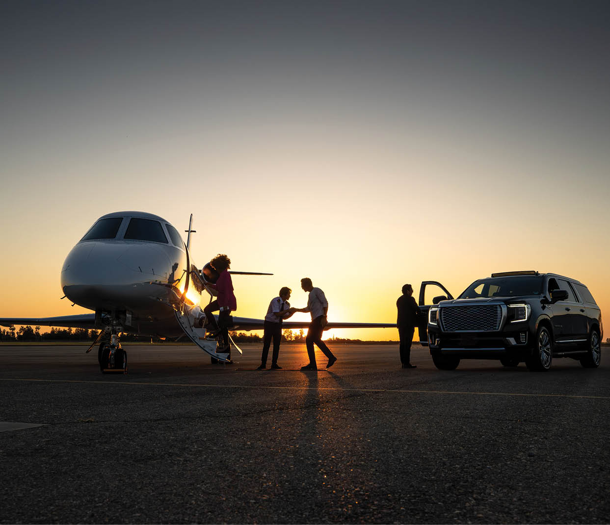 A young Asian pilot welcomes passengers into private jet at dusk.